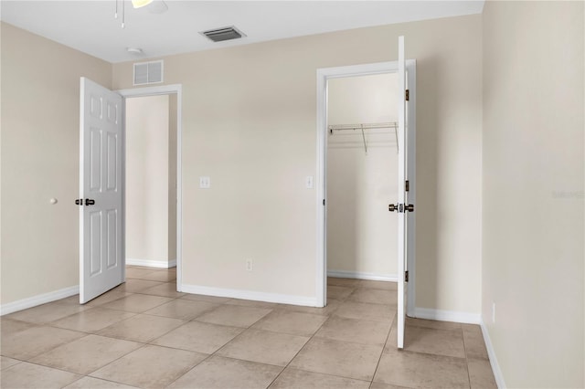 unfurnished bedroom featuring ceiling fan, a walk in closet, a closet, and light tile patterned floors