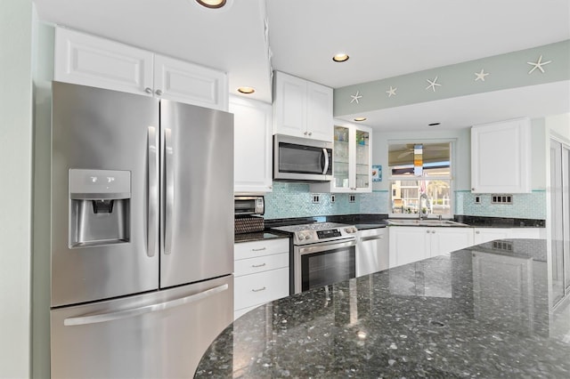 kitchen featuring sink, tasteful backsplash, dark stone counters, stainless steel appliances, and white cabinets