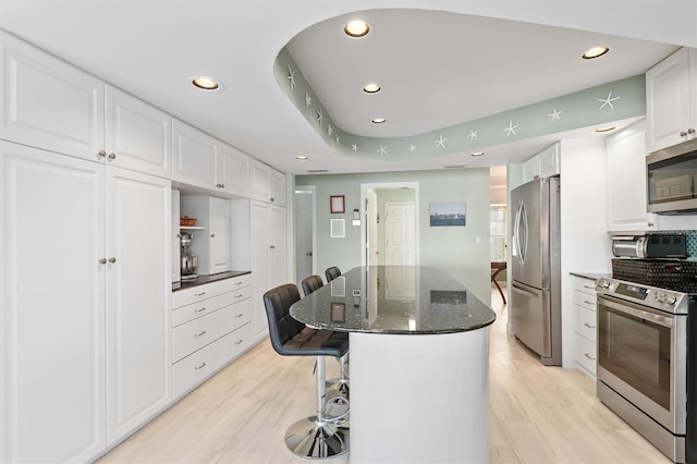 kitchen featuring a kitchen island, a breakfast bar area, white cabinets, dark stone counters, and stainless steel appliances