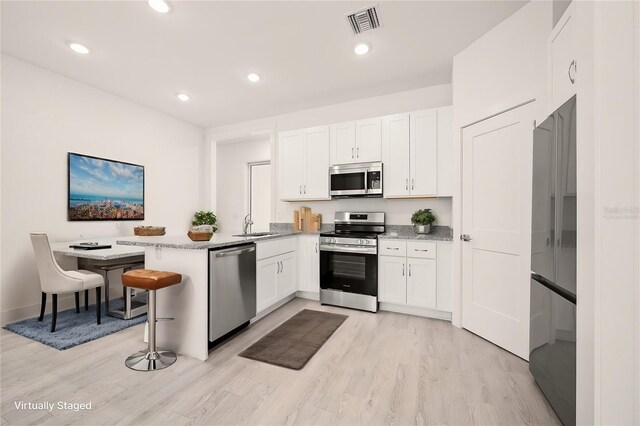 kitchen featuring appliances with stainless steel finishes, a breakfast bar, white cabinets, kitchen peninsula, and light hardwood / wood-style flooring