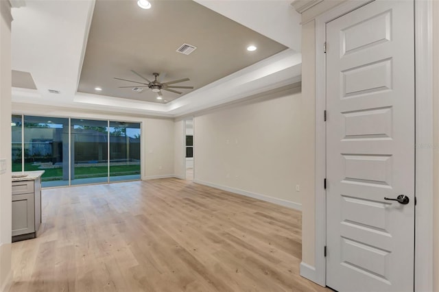 unfurnished living room with ceiling fan, floor to ceiling windows, a tray ceiling, and light hardwood / wood-style flooring