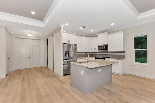 kitchen with appliances with stainless steel finishes, sink, white cabinets, a kitchen island with sink, and light stone countertops