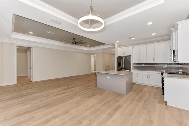 kitchen featuring white cabinetry, appliances with stainless steel finishes, a raised ceiling, and a kitchen island with sink