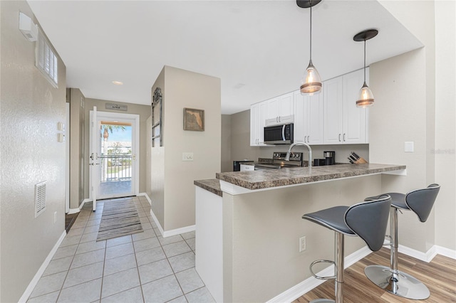 kitchen featuring appliances with stainless steel finishes, decorative light fixtures, white cabinetry, a kitchen breakfast bar, and kitchen peninsula