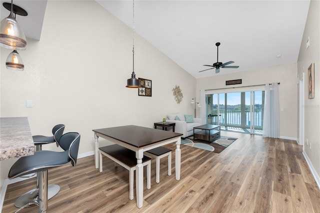 dining room with wood-type flooring, high vaulted ceiling, ceiling fan, and a water view