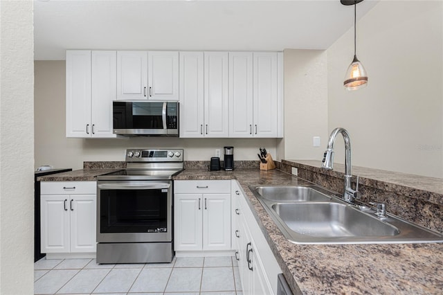 kitchen featuring sink, light tile patterned floors, appliances with stainless steel finishes, white cabinetry, and decorative light fixtures