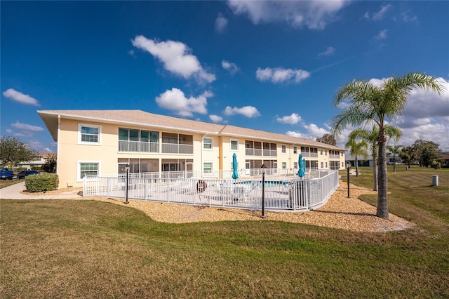 rear view of property featuring a yard, fence, a community pool, and stucco siding