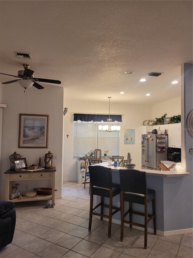 kitchen featuring light tile patterned flooring, a breakfast bar, high end refrigerator, hanging light fixtures, and kitchen peninsula