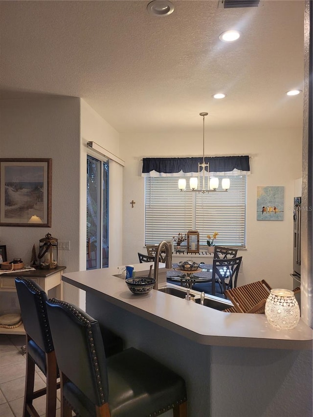 kitchen featuring sink, a breakfast bar, hanging light fixtures, a textured ceiling, and tile patterned floors