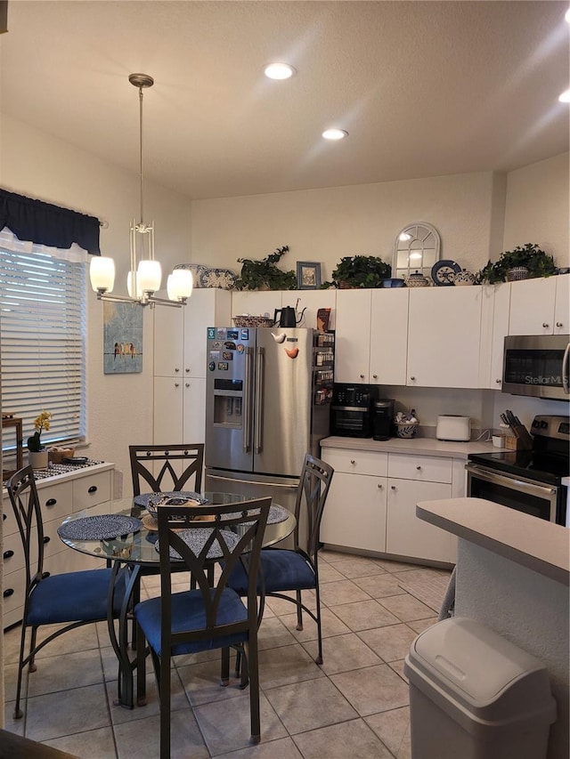 kitchen featuring light tile patterned floors, appliances with stainless steel finishes, hanging light fixtures, a notable chandelier, and white cabinets