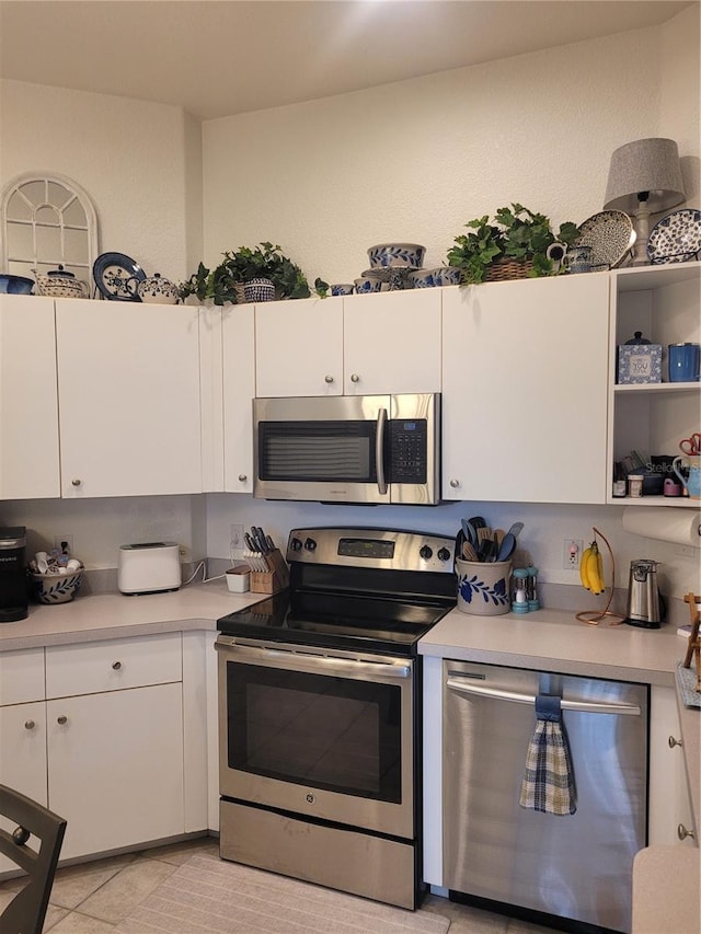 kitchen with stainless steel appliances, white cabinetry, and light tile patterned flooring