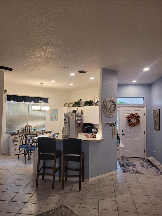 kitchen featuring high end refrigerator, white cabinets, a kitchen bar, light tile patterned floors, and kitchen peninsula