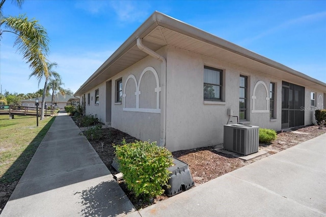 view of side of property with fence, central AC unit, and stucco siding