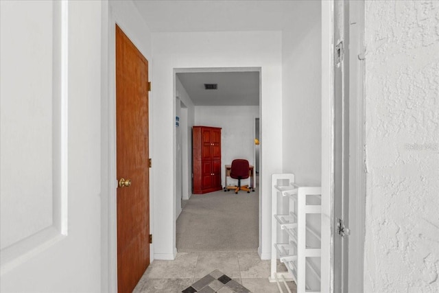 corridor with baseboards, visible vents, and light colored carpet