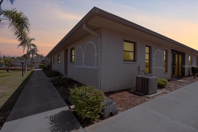 view of side of home featuring fence, central AC, and stucco siding