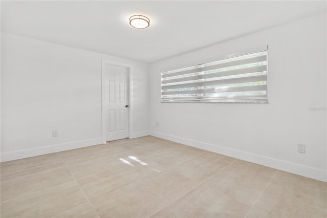 empty room with light tile patterned floors, a wealth of natural light, and baseboards