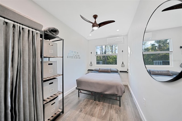 bedroom featuring ceiling fan, a wall mounted AC, and light hardwood / wood-style flooring