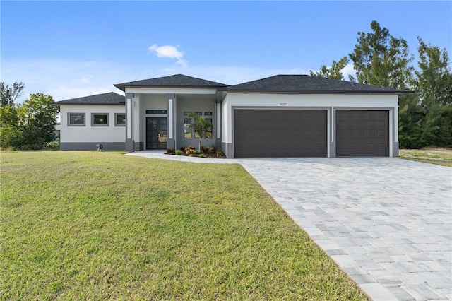 prairie-style home featuring a garage, decorative driveway, a front yard, and stucco siding