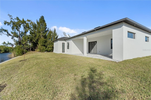 rear view of property featuring a lawn, a patio area, and stucco siding