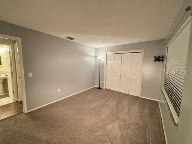 unfurnished bedroom featuring ensuite bath, dark carpet, and a closet