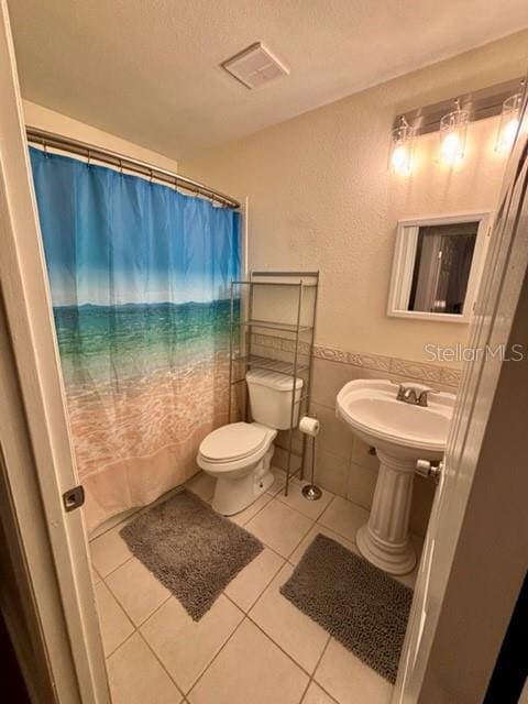 bathroom featuring toilet, a textured ceiling, tile walls, a shower with shower curtain, and tile patterned flooring