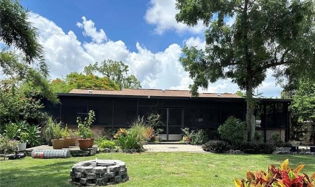 rear view of house featuring a sunroom, a lawn, and a fire pit