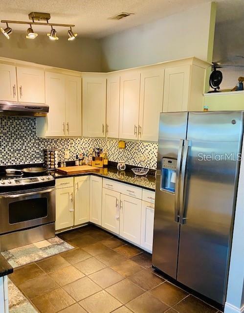 18085 Wintergarden Ave, Port Charlotte, FL 33948 - kitchen with appliances with stainless steel finishes, under cabinet range hood, backsplash, white cabinets, and a textured ceiling