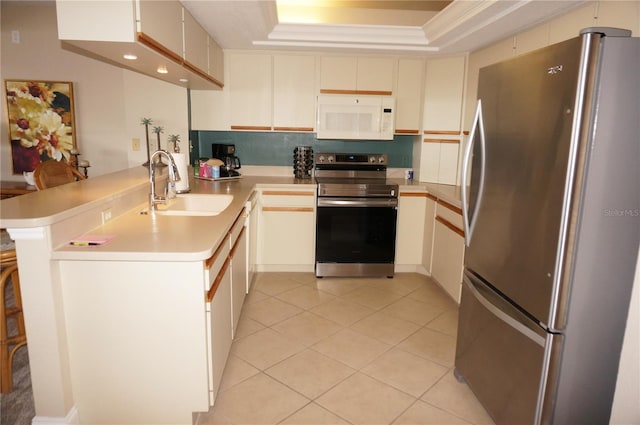 kitchen with light tile patterned flooring, a raised ceiling, sink, kitchen peninsula, and stainless steel appliances