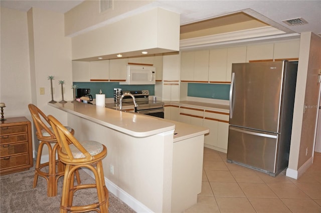 kitchen with light tile patterned flooring, appliances with stainless steel finishes, a kitchen bar, kitchen peninsula, and cream cabinetry