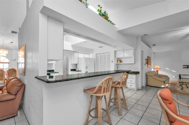 kitchen featuring light tile patterned floors, white fridge with ice dispenser, kitchen peninsula, and white cabinets