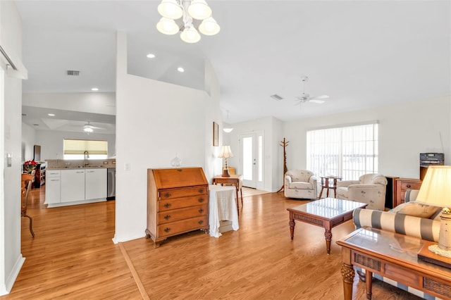 living room with ceiling fan with notable chandelier, lofted ceiling, light hardwood / wood-style floors, and sink