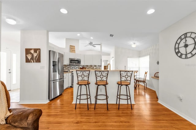 kitchen featuring tasteful backsplash, lofted ceiling, white cabinets, a kitchen breakfast bar, and stainless steel appliances