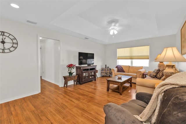 living room with ceiling fan, a tray ceiling, and light hardwood / wood-style flooring