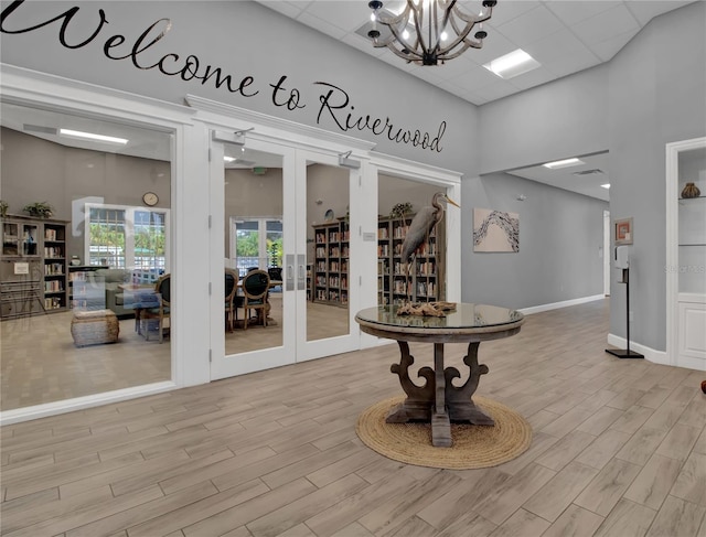 interior space with light wood-type flooring, french doors, a chandelier, and a high ceiling