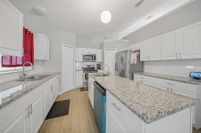 kitchen featuring sink, hanging light fixtures, stainless steel appliances, an island with sink, and white cabinets