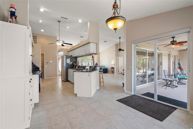 kitchen with stainless steel refrigerator, white cabinetry, a wealth of natural light, a kitchen bar, and vaulted ceiling