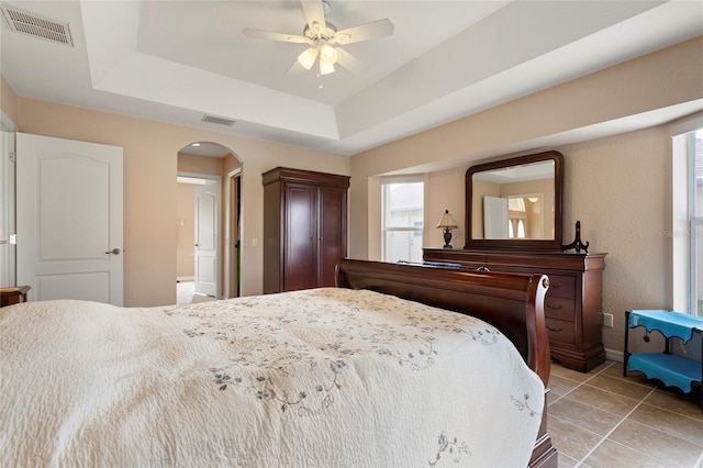 tiled bedroom with ceiling fan and a tray ceiling