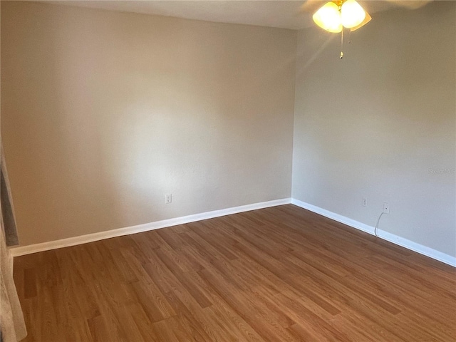 spare room featuring dark wood-type flooring, a ceiling fan, and baseboards