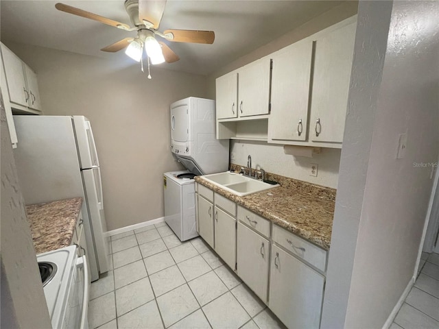 kitchen with light tile patterned flooring, white appliances, a sink, baseboards, and stacked washer and clothes dryer