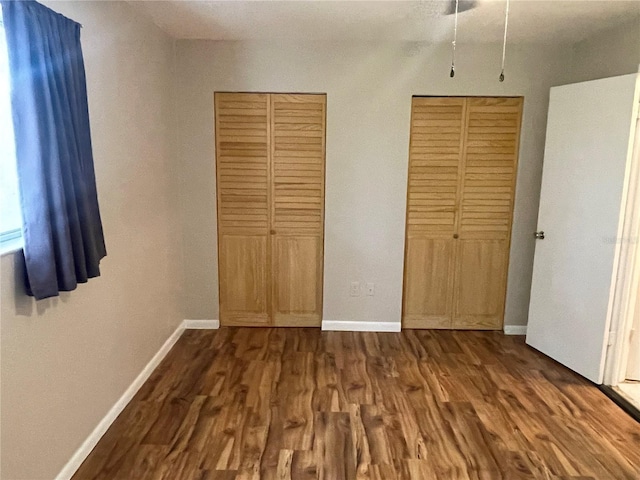 unfurnished bedroom featuring dark wood finished floors, baseboards, and two closets