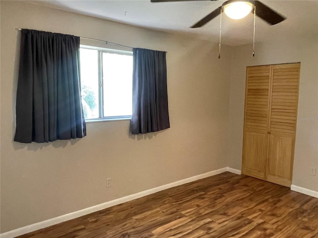 unfurnished bedroom featuring ceiling fan, baseboards, dark wood finished floors, and a closet