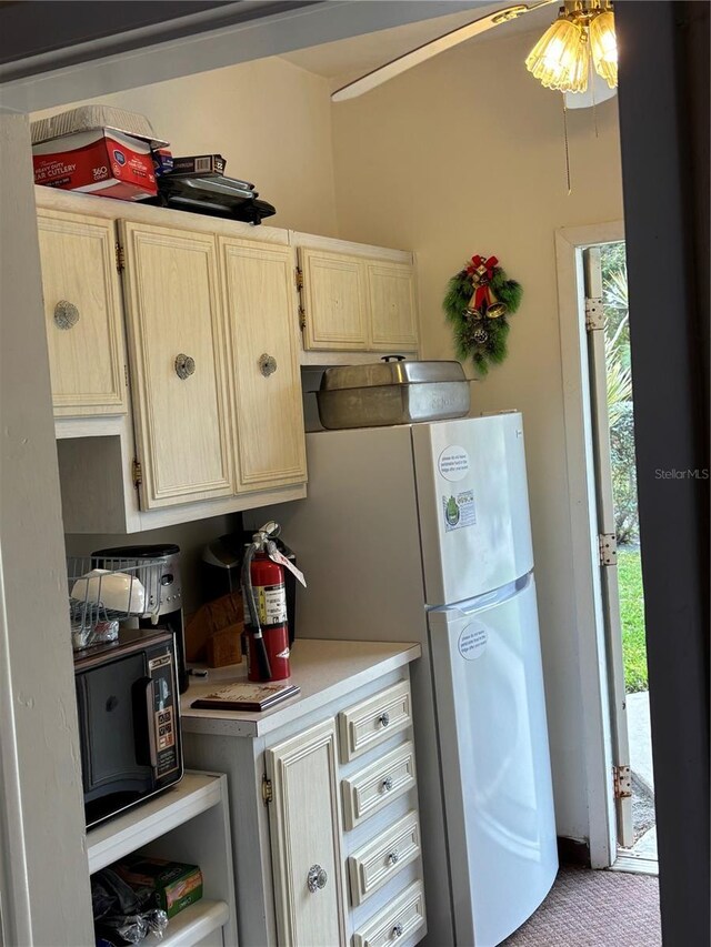 kitchen featuring black microwave, light countertops, light brown cabinetry, and freestanding refrigerator