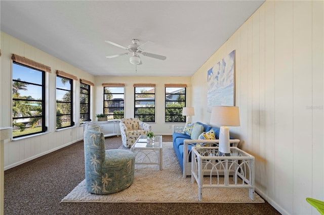 living room featuring carpet flooring, wooden walls, and ceiling fan