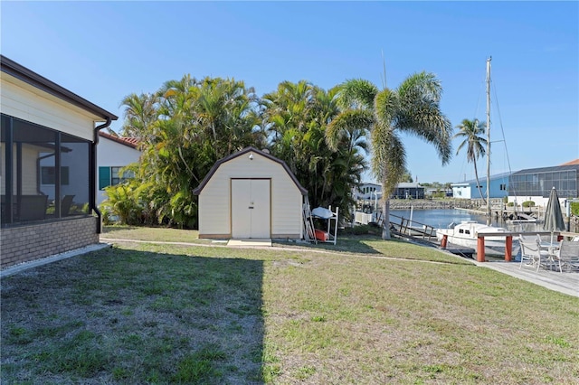 view of yard with a water view, a storage shed, a dock, and a sunroom