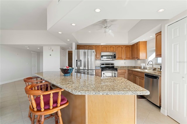 kitchen with a kitchen island, appliances with stainless steel finishes, a breakfast bar area, light tile patterned floors, and a tray ceiling