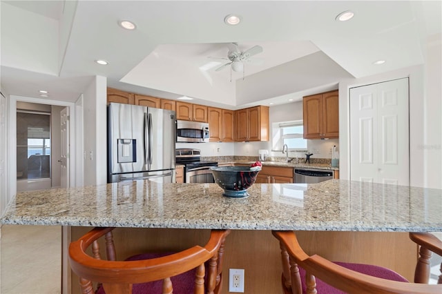 kitchen with sink, a breakfast bar, ceiling fan, stainless steel appliances, and a tray ceiling