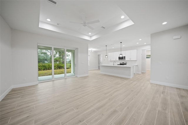 unfurnished living room with a tray ceiling, light hardwood / wood-style flooring, and ceiling fan