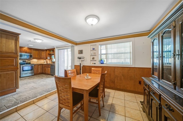 dining area featuring light tile patterned floors, crown molding, and wood walls