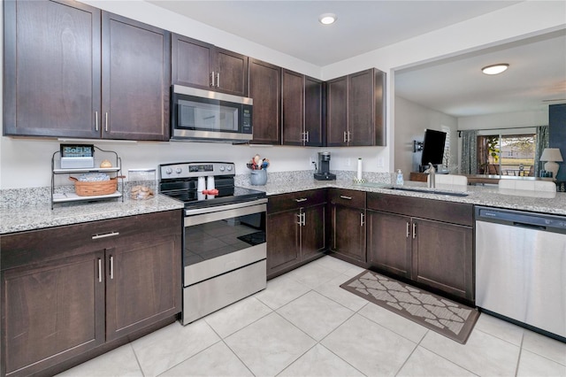 kitchen with light stone counters, appliances with stainless steel finishes, sink, and dark brown cabinets