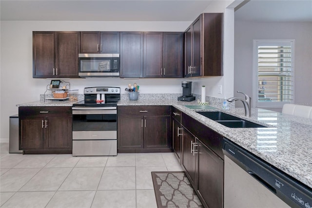 kitchen featuring light tile patterned floors, sink, stainless steel appliances, dark brown cabinetry, and light stone countertops